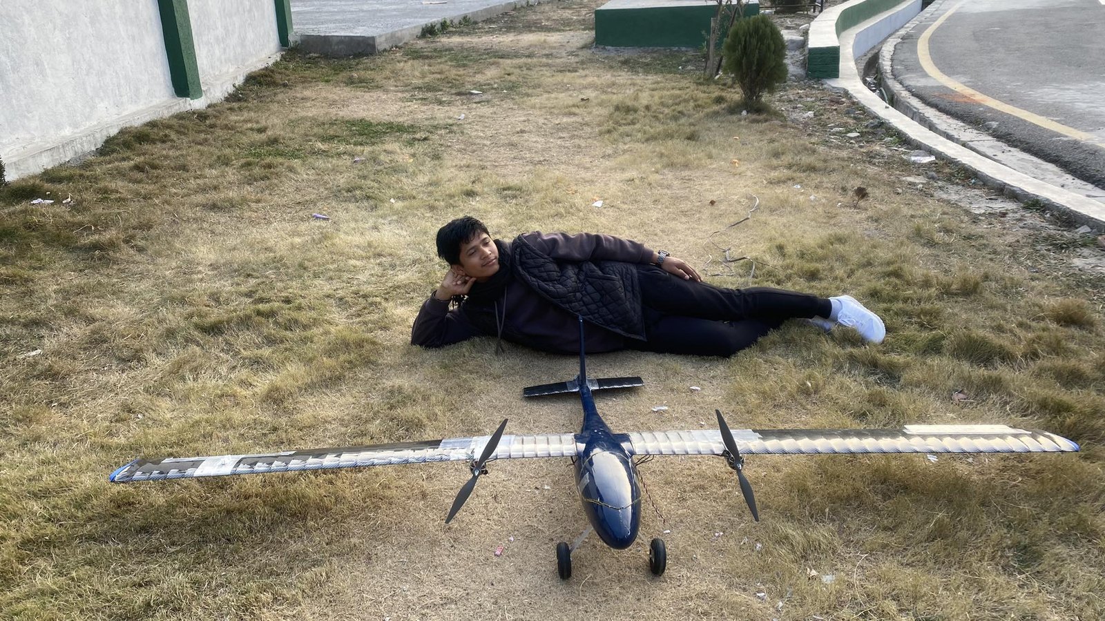 Person lying next to the RC aircraft on grass for scale